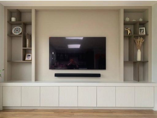 TV wall unit with display shelving and low ribbed door cabinets Modern living room with a wall-mounted TV, floating shelves, and a low-profile cabinet.