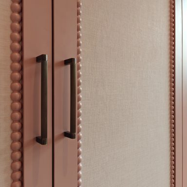 Antique Rose wardrobe door detail Close-up of a pink cabinet with textured surface and black handles.