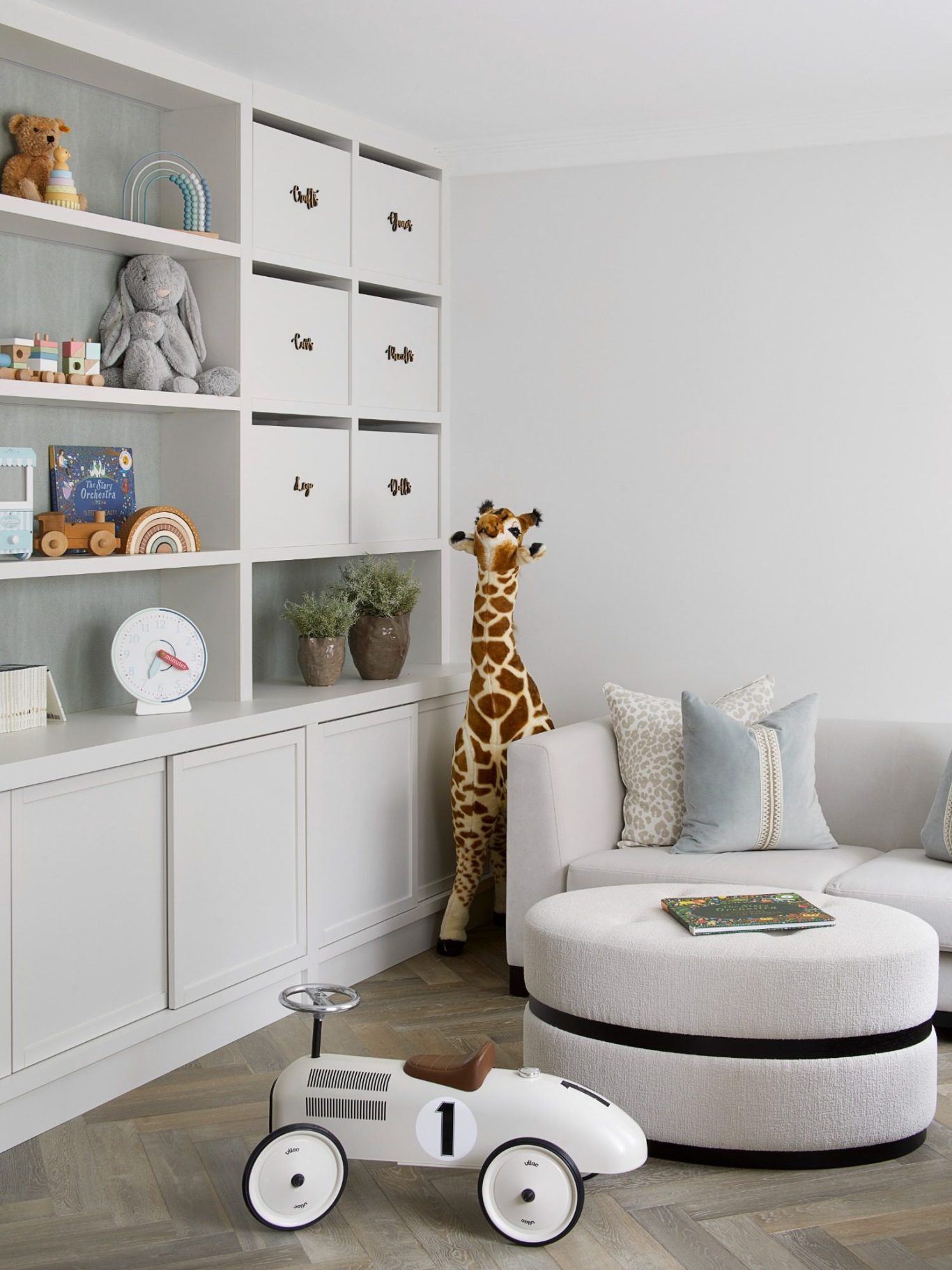 Grey White storage with sliding doors and open display shelving Bright, modern living room with a plush sofa, toy car, and a giraffe figurine.